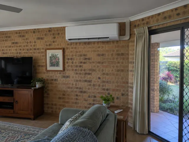 Living room with a wall-mounted split system on a brick wall, curtains and sliding door in Merrimac