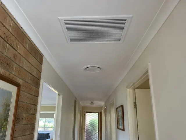 Ceiling return-air grille and round outlet in a narrow hallway with brick feature wall in Worongary