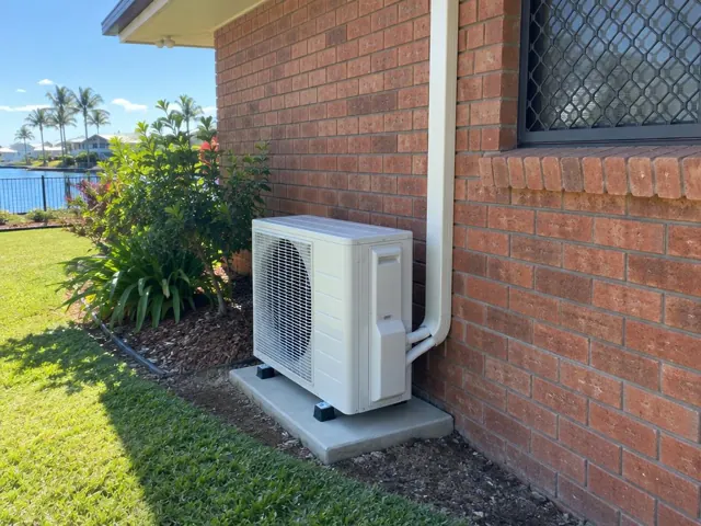 Outdoor air conditioner unit on a concrete pad beside a brick house wall in Broadbeach Waters